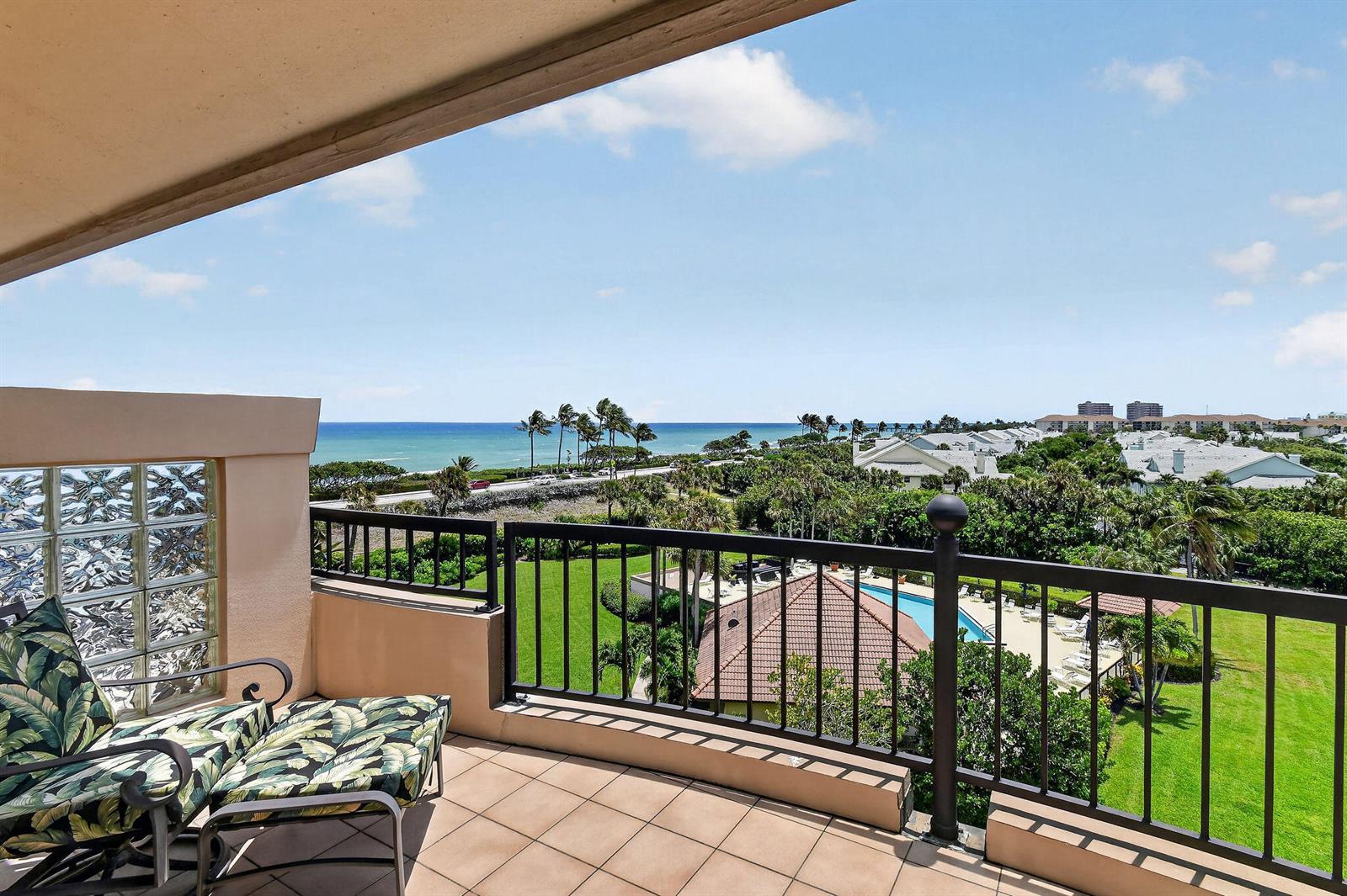 A balcony with a patterned chair overlooks a swimming pool, lush greenery, and the ocean — 101 Ocean Bluffs Boulevard # 504, Jupiter FL 33477, JUPITER, FL