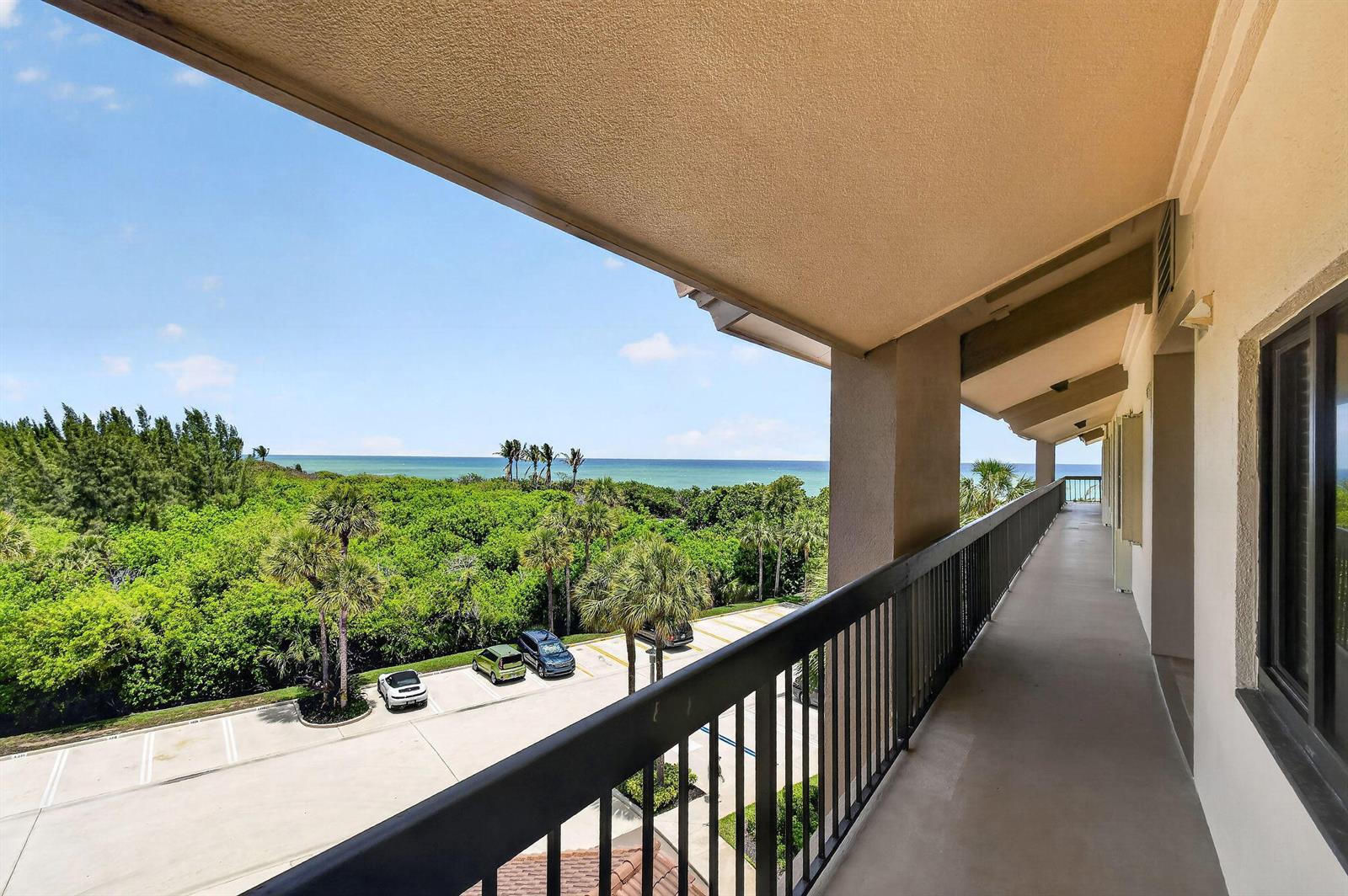 A covered balcony overlooks a parking lot, lush green trees, and the ocean — 101 Ocean Bluffs Boulevard # 504, Jupiter FL 33477, JUPITER, FL