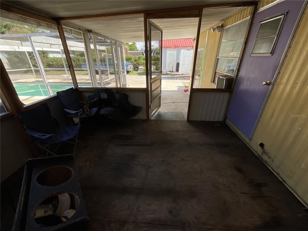 A screened-in porch with plywood flooring, folding chairs, and a view of a swimming pool — 702 JERSEY COURT, DUNDEE, FL