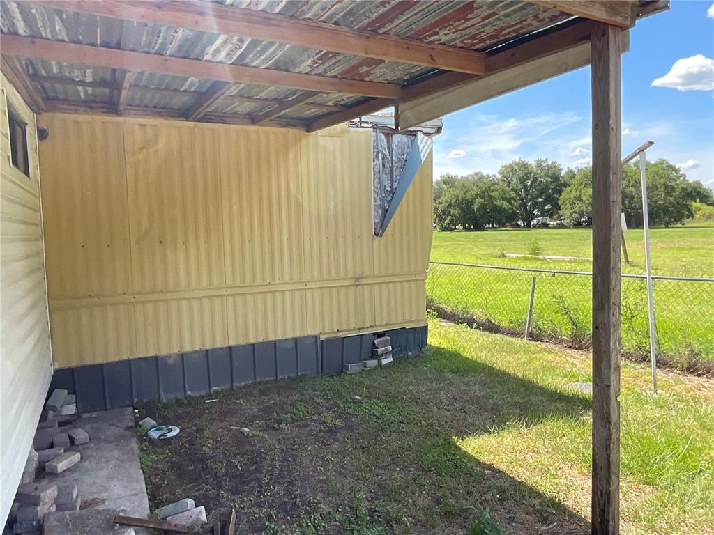 An exterior view of a mobile home with a covered patio and damaged metal siding — 702 JERSEY COURT, DUNDEE, FL