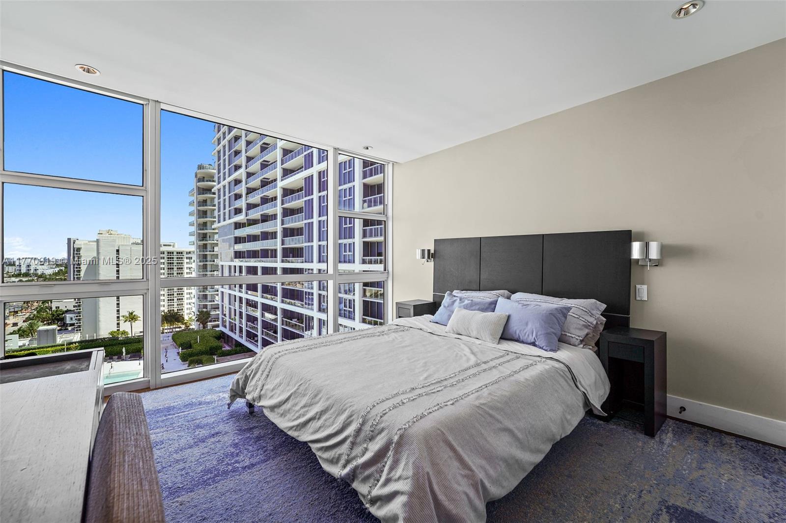 A bedroom with a bed, nightstands, and floor-to-ceiling windows overlooking a city skyline — 6801 Collins Ave, Miami Beach FL 33141, MIAMI BEACH, FL
