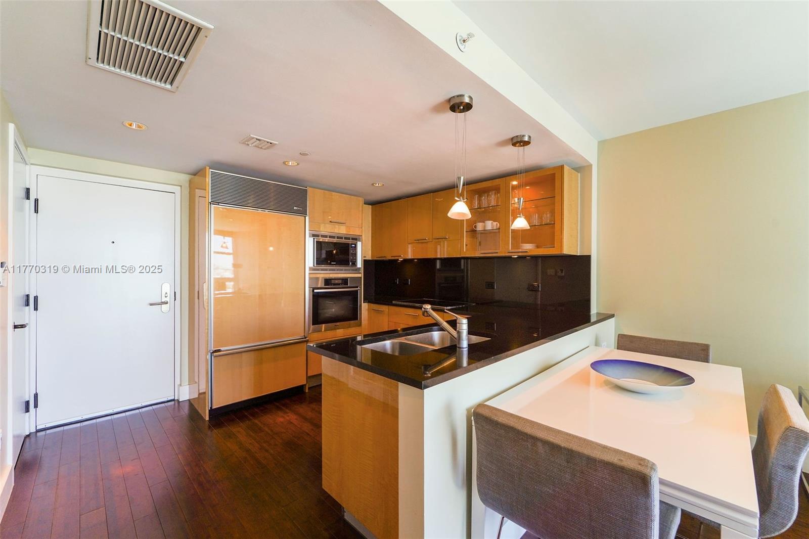 A kitchen features light wood cabinetry, black countertops, stainless steel appliances, and an adjacent dining area — 6801 Collins Ave, Miami Beach FL 33141, MIAMI BEACH, FL