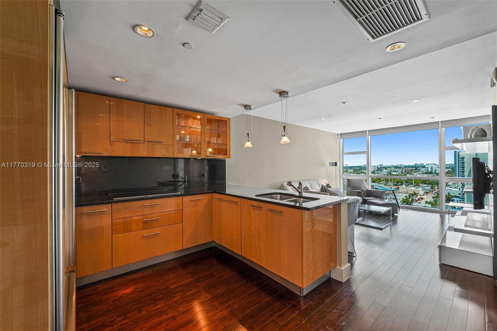 A kitchen with wood cabinets and black countertops overlooks a living area and city view — 6801 Collins Ave, Miami Beach FL 33141, MIAMI BEACH, FL