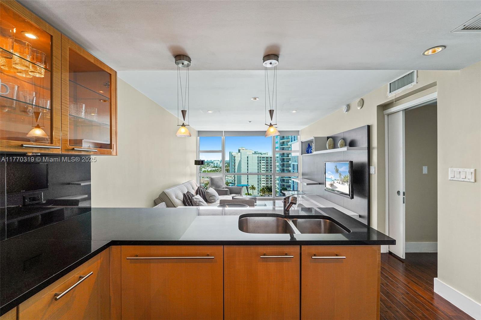 A kitchen with dark countertops and wood cabinets overlooks a living area with floor-to-ceiling windows — 6801 Collins Ave, Miami Beach FL 33141, MIAMI BEACH, FL