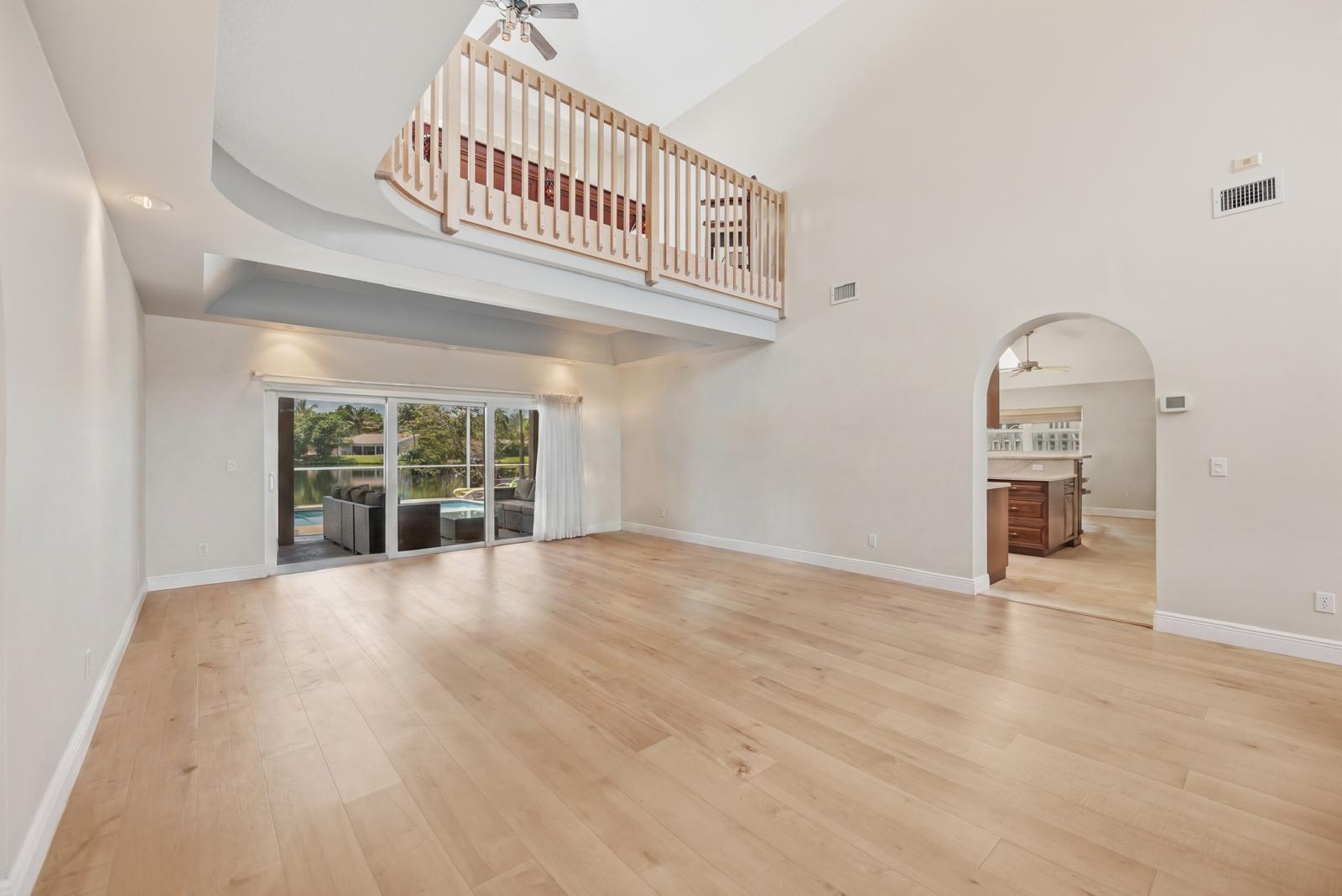 An empty living room with light wood floors, a vaulted ceiling, and a loft balcony — 9410 Sea Turtle Manor, Plantation FL 33324, PLANTATION, FL