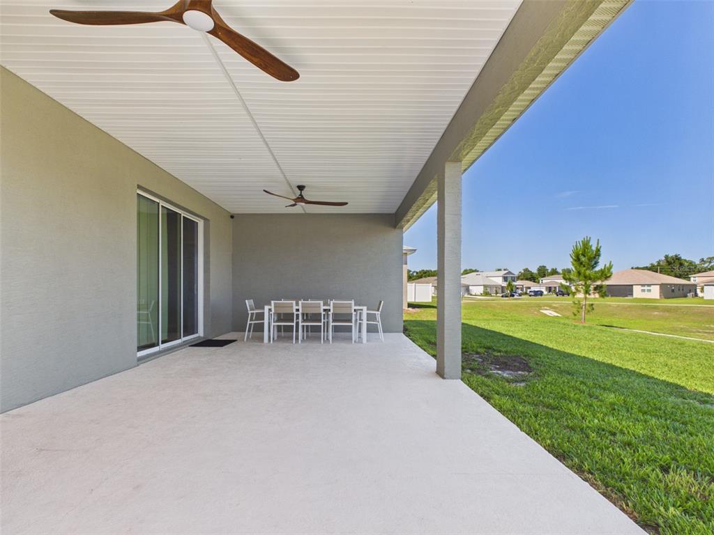 A covered concrete patio features a ceiling fan and a dining set overlooking a lawn — 7813 SW 56TH PLACE, OCALA, FL