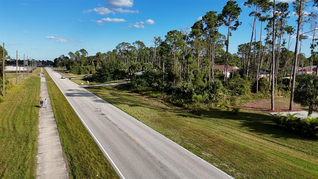 An aerial view shows a paved road, a sidewalk with two pedestrians, and wooded land — E PRICE BOULEVARD, NORTH PORT, FL