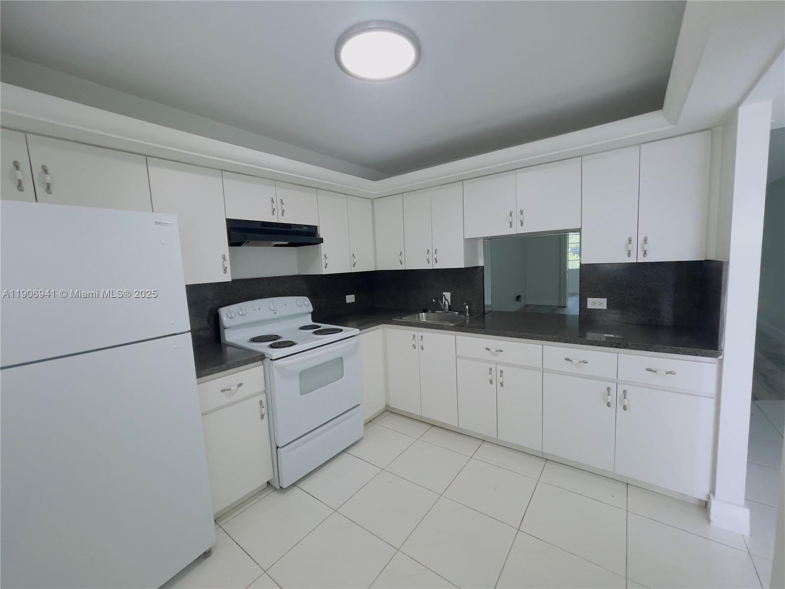 A kitchen features white cabinets, white appliances, dark countertops, and light-colored tile flooring — 443 NE 195th St # 338, Miami FL 33179, MIAMI, FL
