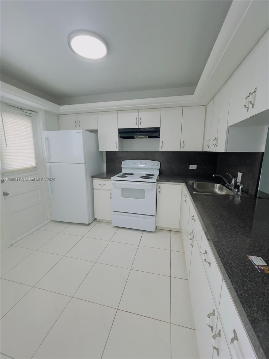 A kitchen features white cabinets, white appliances, dark countertops, and light-colored floor tiles — 443 NE 195th St # 338, Miami FL 33179, MIAMI, FL