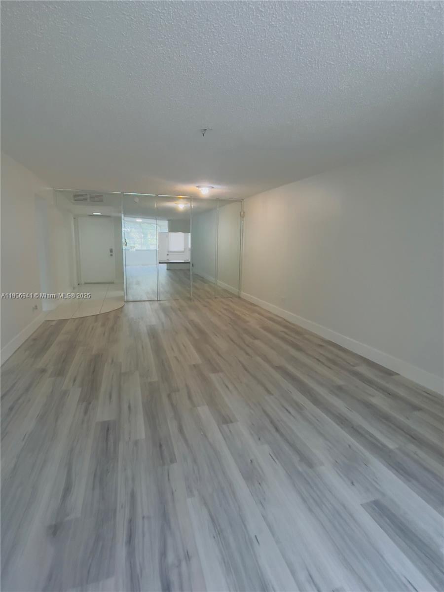 An empty room features light-colored wood-look flooring and a wall of floor-to-ceiling mirrors — 443 NE 195th St # 338, Miami FL 33179, MIAMI, FL