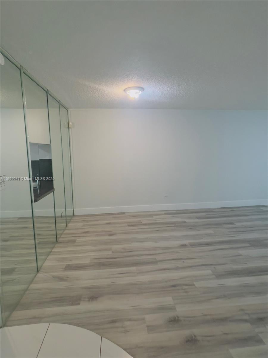 A room with light wood-look flooring, a white wall, and a mirrored closet wall — 443 NE 195th St # 338, Miami FL 33179, MIAMI, FL