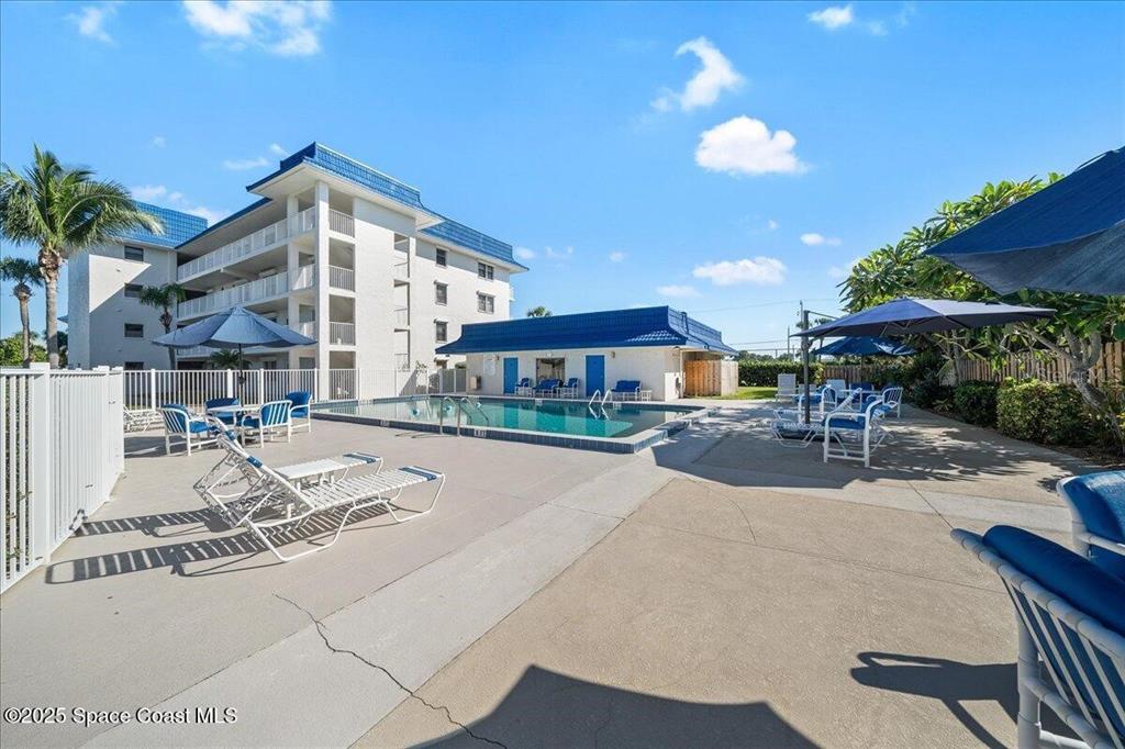 An outdoor swimming pool area with lounge chairs, umbrellas, and a multi-story building — 2160 N HIGHWAY A1A UNIT 202, INDIALANTIC, FL