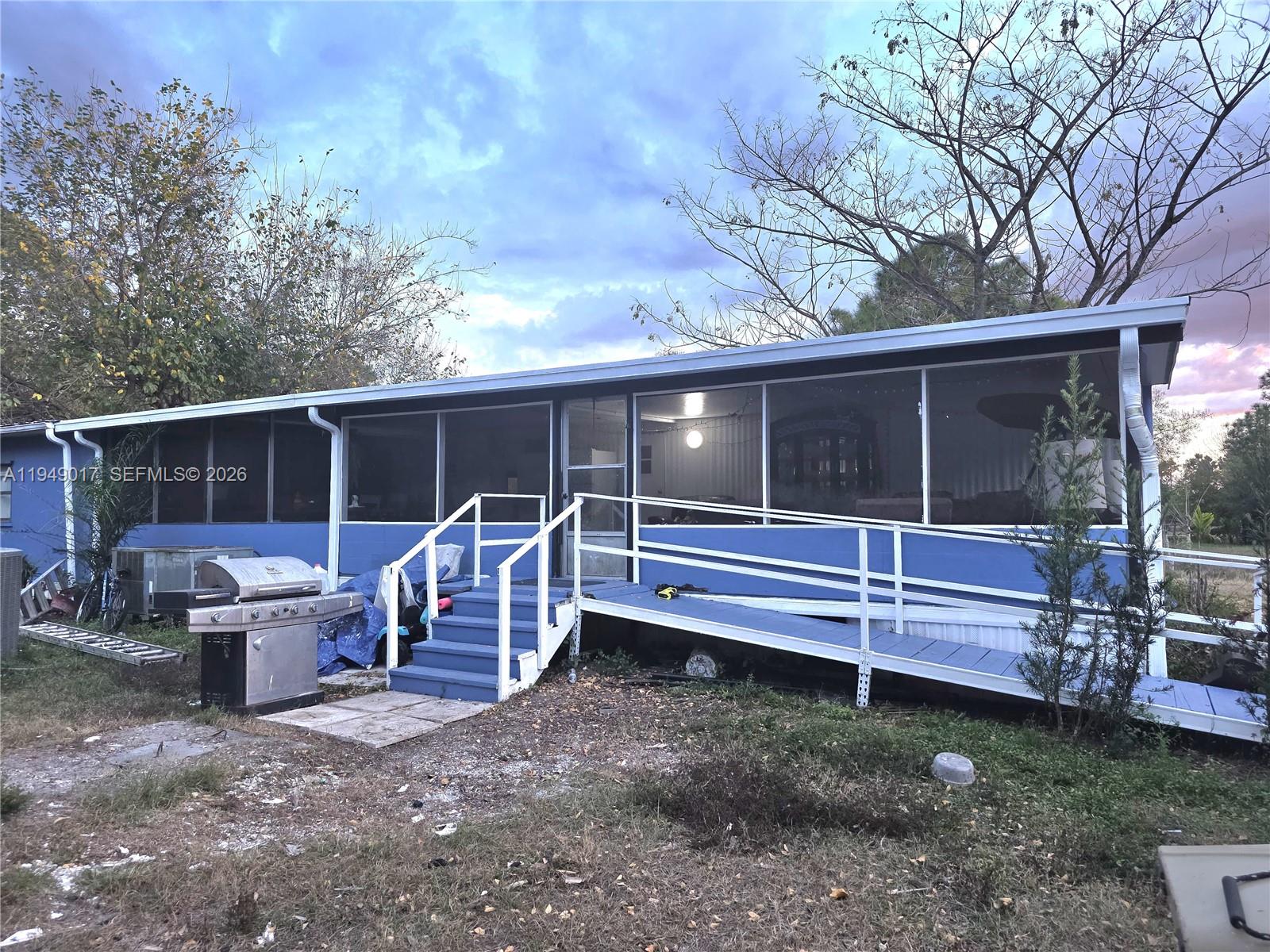 A blue mobile home features a screened-in porch, a wooden staircase, and a wheelchair ramp — 575 VERO AVE, Clewiston FL 33440, CLEWISTON, FL