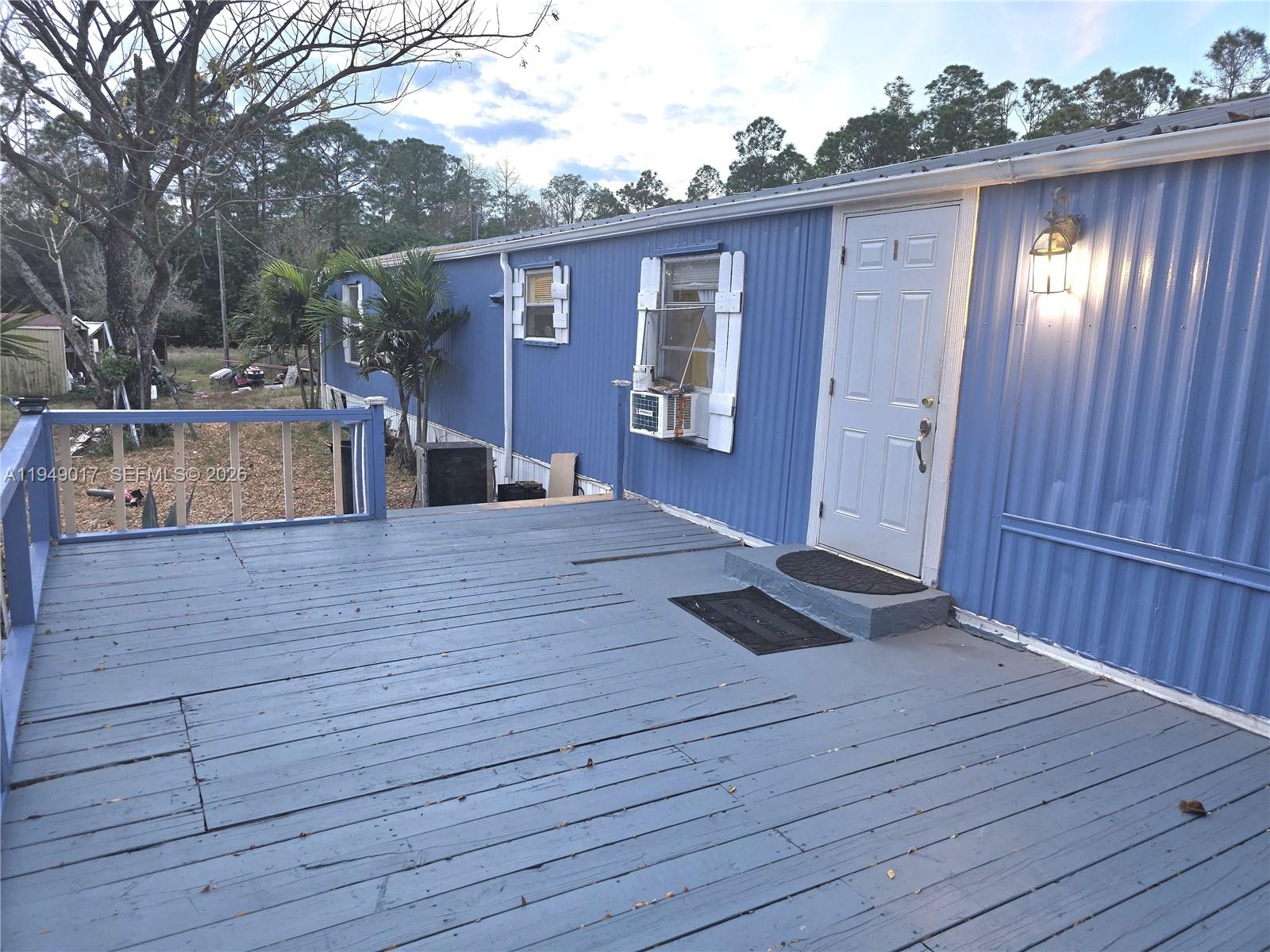 A blue mobile home features a wooden deck with a railing and a white door — 575 VERO AVE, Clewiston FL 33440, CLEWISTON, FL