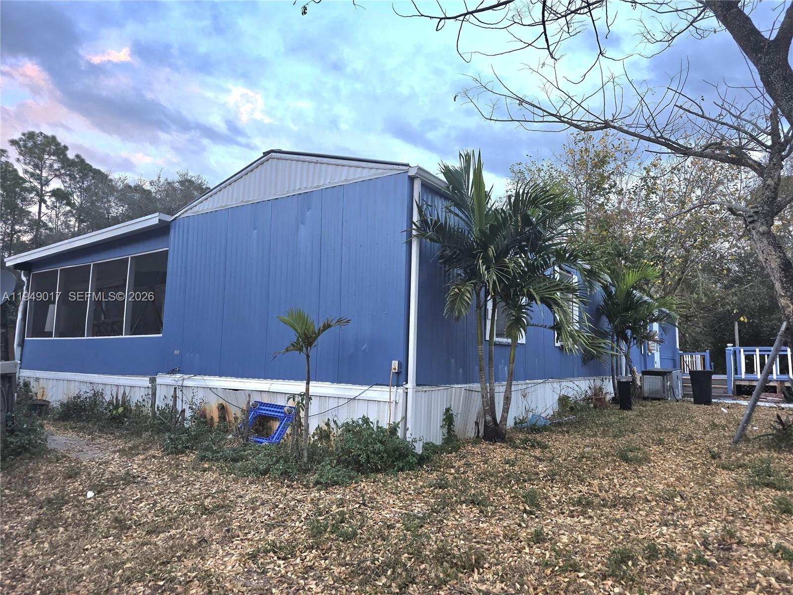 A blue mobile home with a screened-in porch sits on a lot with palm trees — 575 VERO AVE, Clewiston FL 33440, CLEWISTON, FL