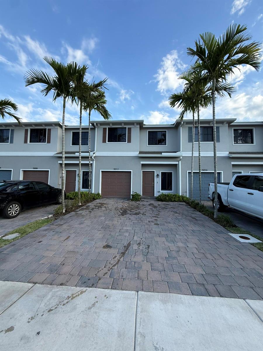 A row of two-story townhomes with gray siding, brown garage doors, and palm trees in front — 5012 Elderberry Street, Haverhill FL 33415, HAVERHILL, FL