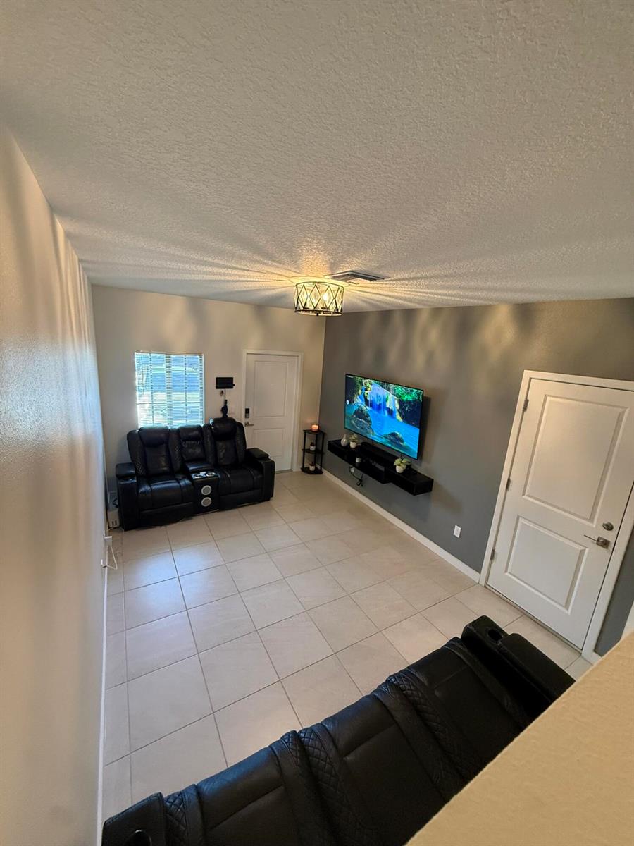A living room features light tile flooring, a mounted television, and two black leather sofas — 5012 Elderberry Street, Haverhill FL 33415, HAVERHILL, FL