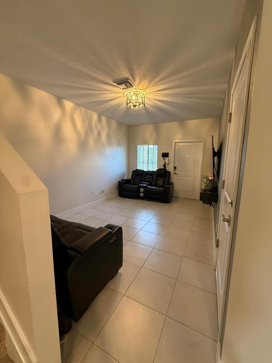 A living room features light tile flooring, two black leather sofas, and a ceiling light fixture — 5012 Elderberry Street, Haverhill FL 33415, HAVERHILL, FL