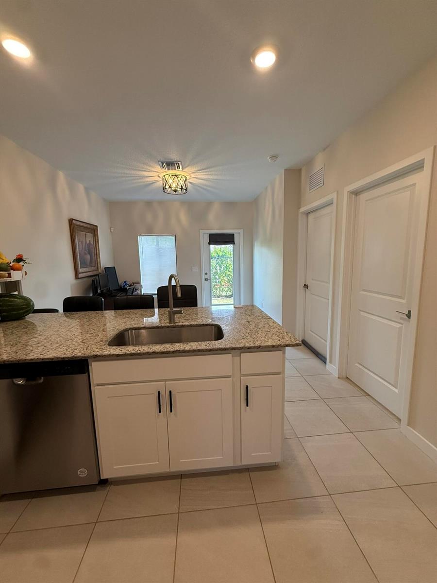 A kitchen island with a granite countertop and stainless steel sink sits before a dining area — 5012 Elderberry Street, Haverhill FL 33415, HAVERHILL, FL