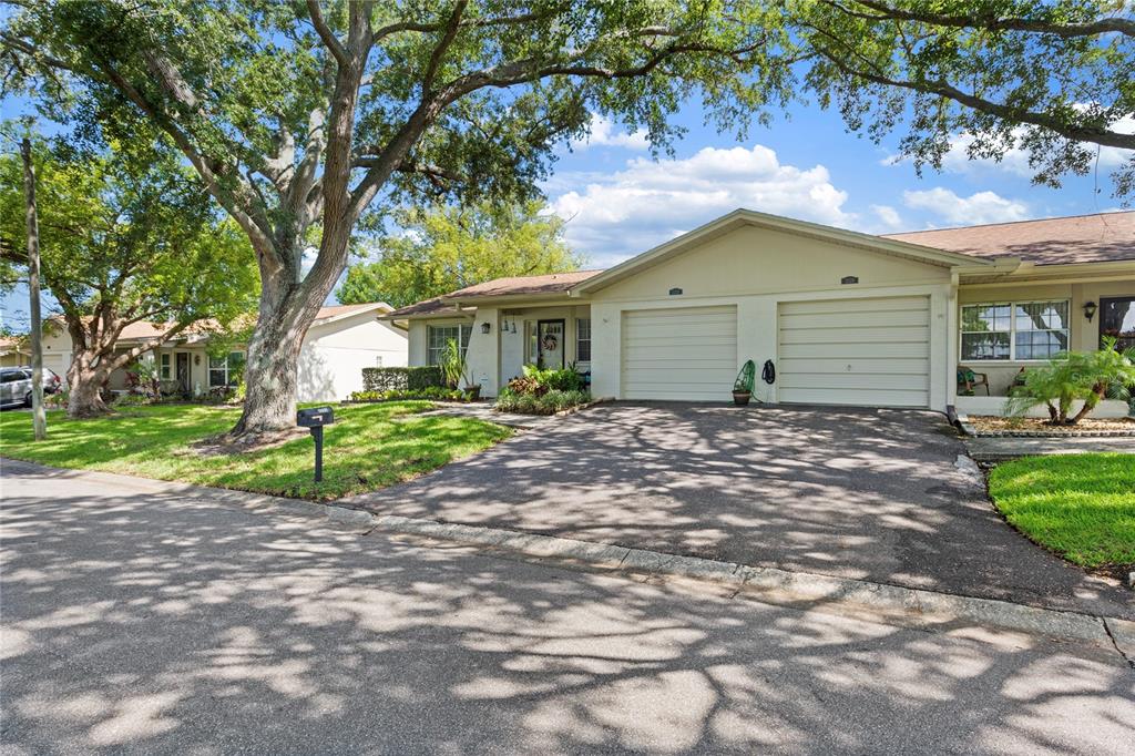 A single-story duplex with two garage doors, a paved driveway, and large shade trees — 2220 MARSHALL DRIVE, DUNEDIN, FL