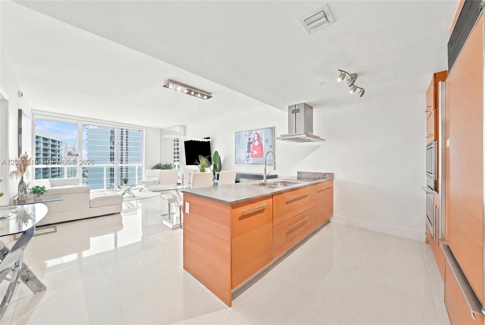 A modern kitchen with wood cabinets and a stone island opens into a living area — 485 Brickell Ave # 3707, Miami FL 33131, MIAMI, FL