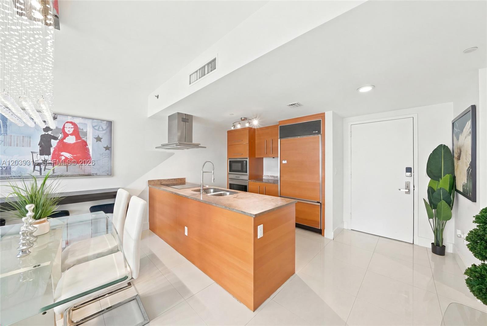 A modern kitchen features wood cabinetry, a central island with a sink, and tile flooring — 485 Brickell Ave # 3707, Miami FL 33131, MIAMI, FL