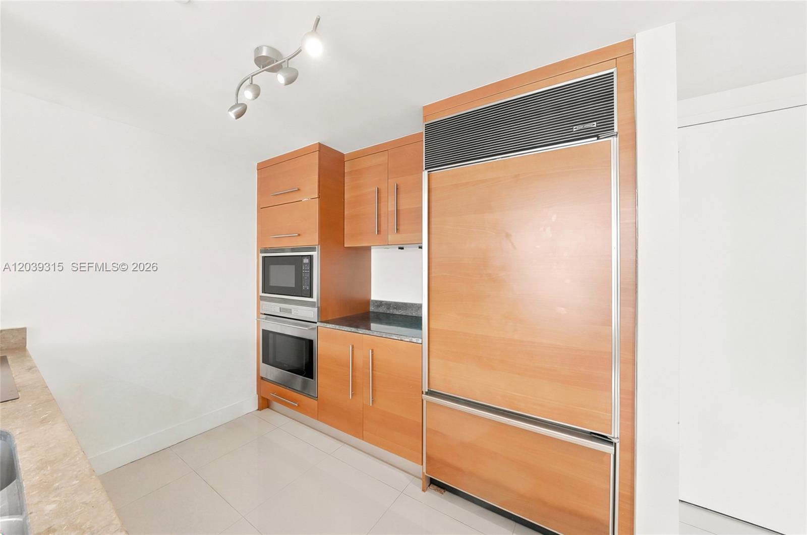 A modern kitchen features light wood cabinetry, stainless steel appliances, and a built-in refrigerator — 485 Brickell Ave # 3707, Miami FL 33131, MIAMI, FL