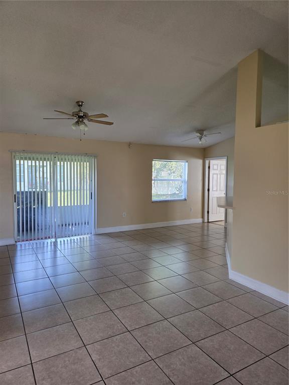 An open living area features beige walls, tile flooring, two ceiling fans, and sliding glass doors — 953 LOUVRE COURT, KISSIMMEE, FL