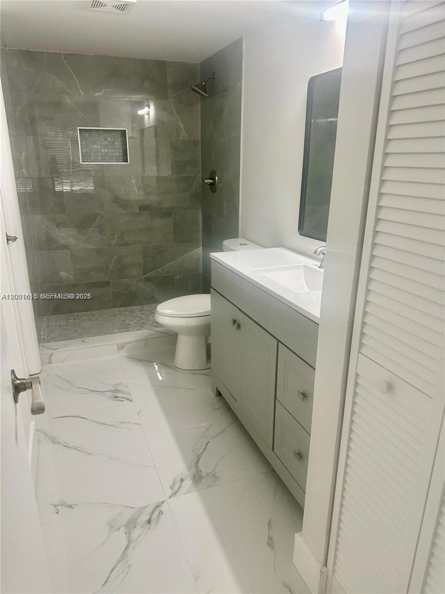 A bathroom features a walk-in shower with gray tile, a white vanity, and marble-patterned flooring — 4166 Inverrary Dr # 210, Lauderhill FL 33319, LAUDERHILL, FL