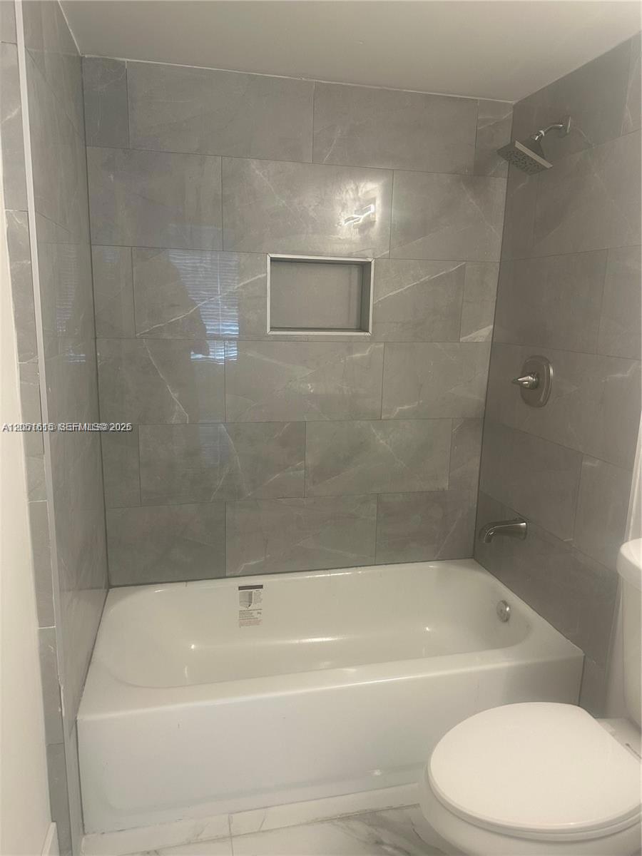 A bathroom features a white bathtub with gray tiled walls and a built-in shower niche — 4166 Inverrary Dr # 210, Lauderhill FL 33319, LAUDERHILL, FL