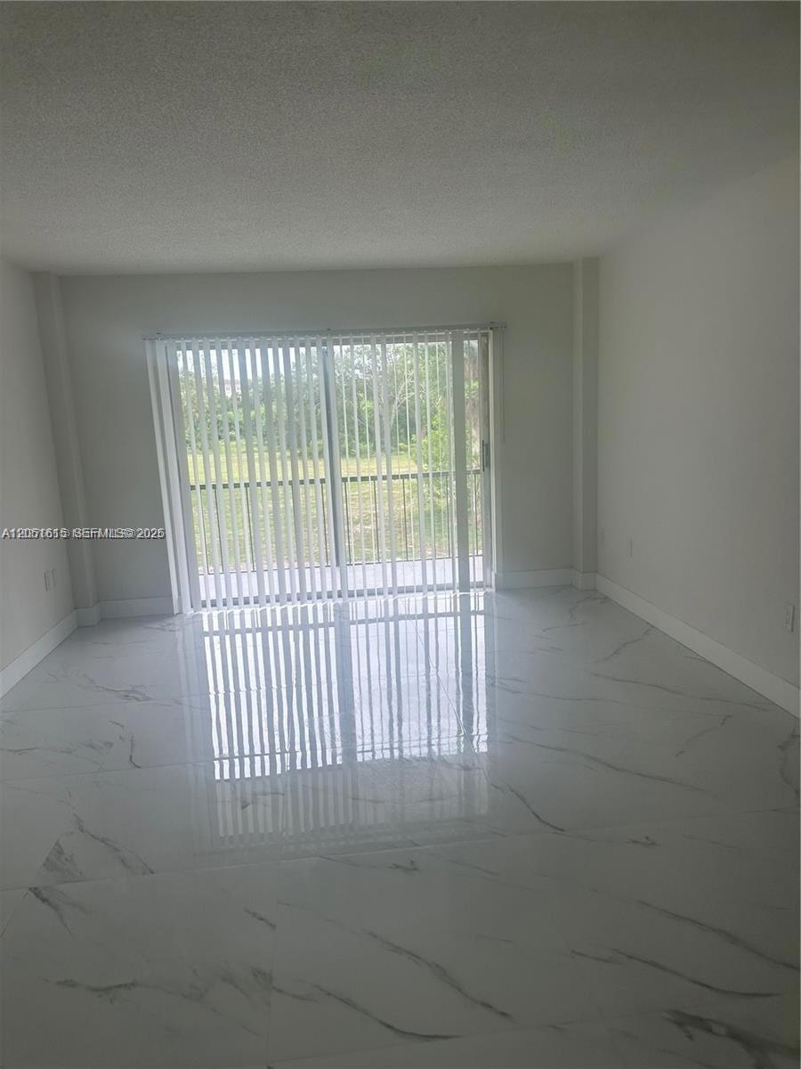A bright, empty room features white marble-look tile flooring and a sliding glass balcony door — 4166 Inverrary Dr # 210, Lauderhill FL 33319, LAUDERHILL, FL