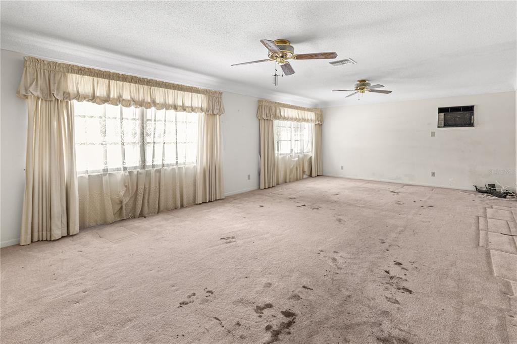 A large, empty living room features beige wall-to-wall carpeting, two ceiling fans, and window curtains — 5331 98TH WAY N, ST PETERSBURG, FL
