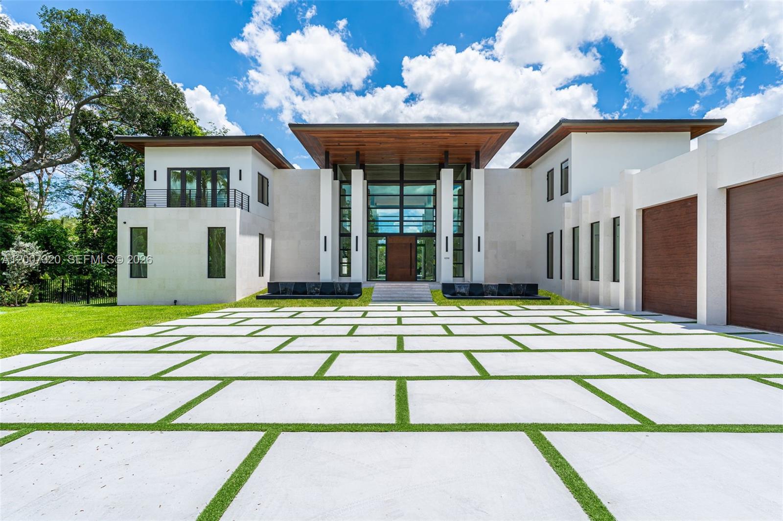 A modern two-story house features a large glass entryway, wood accents, and a paved driveway — 6290 Chapman Field Dr, Pinecrest FL 33156, PINECREST, FL