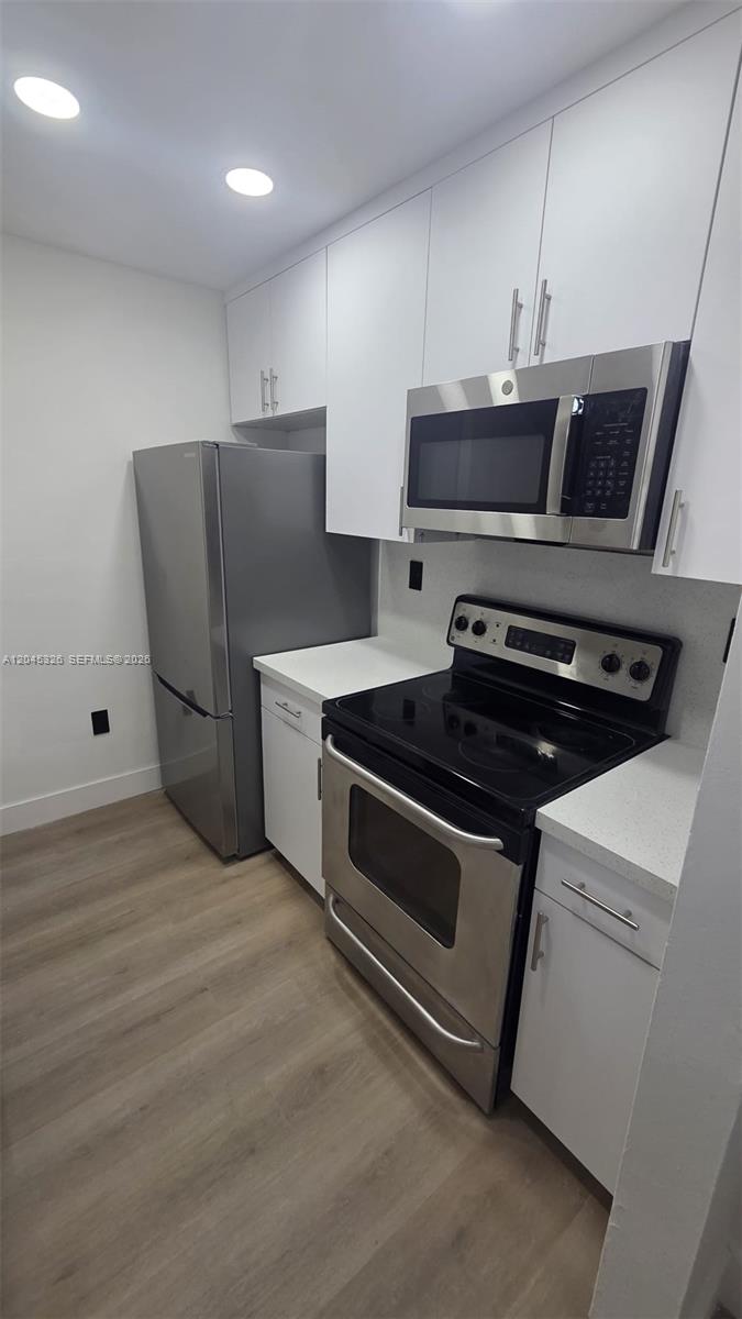 A modern kitchen features white cabinets, stainless steel appliances, and light wood-look flooring — 7125 NW 186th St # B201, Hialeah FL 33015, HIALEAH, FL