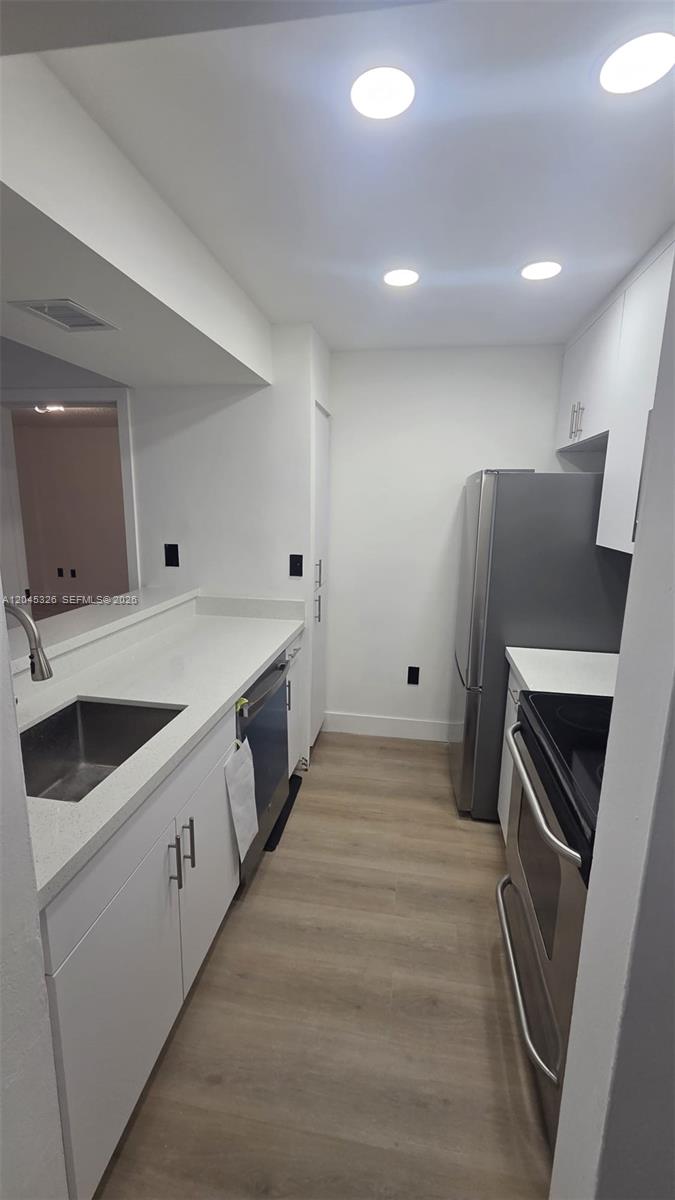 A galley kitchen features white cabinets, stainless steel appliances, and light wood-look flooring — 7125 NW 186th St # B201, Hialeah FL 33015, HIALEAH, FL