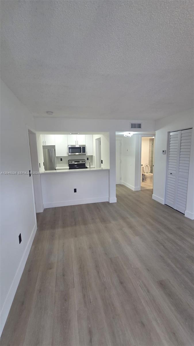 An interior view shows a kitchen with white cabinets and a living area with wood-look flooring — 7125 NW 186th St # B201, Hialeah FL 33015, HIALEAH, FL