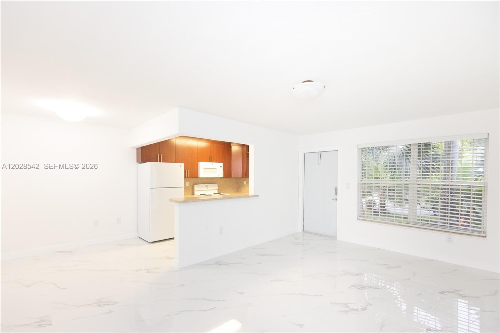 A bright, open-concept kitchen and living area features white marble-style flooring and wood cabinetry — 1060 NE 78th St Rd # 3, Miami FL 33138, MIAMI, FL