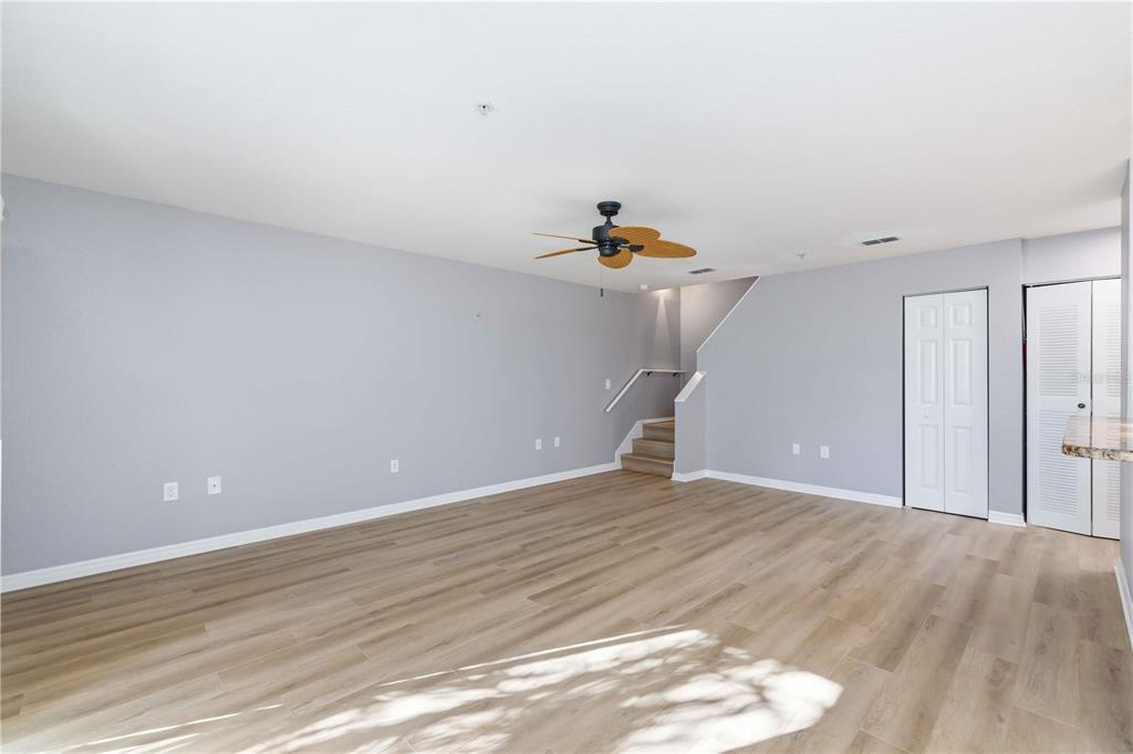 An empty living room features light gray walls, wood-look flooring, a ceiling fan, and stairs — 850 S TAMIAMI TRAIL UNIT 630, SARASOTA, FL