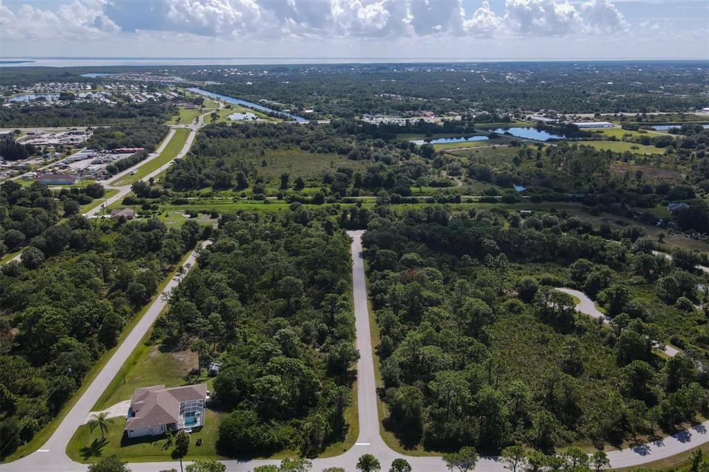 An aerial view shows a paved road leading into a wooded area with a house — 13200 WAFFLE LANE, PORT CHARLOTTE, FL