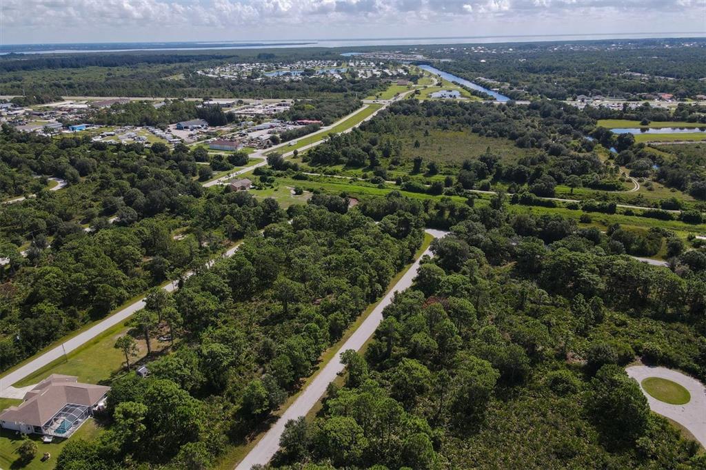 An aerial view shows a residential area with wooded lots, paved roads, and a house — 13200 WAFFLE LANE, PORT CHARLOTTE, FL