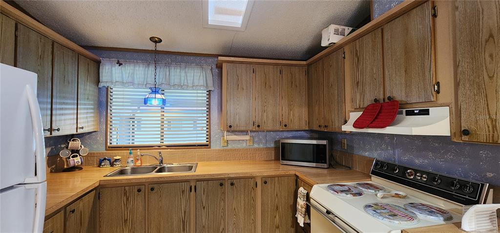 A kitchen features wood-grain cabinets, laminate countertops, a double sink, and a white stove — 2604 MCDANIEL DRIVE, KISSIMMEE, FL