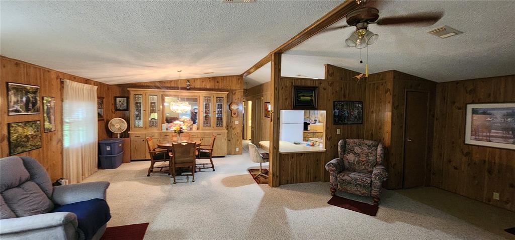 A living room and dining area feature wood-paneled walls, carpeted floors, and a ceiling fan — 2604 MCDANIEL DRIVE, KISSIMMEE, FL