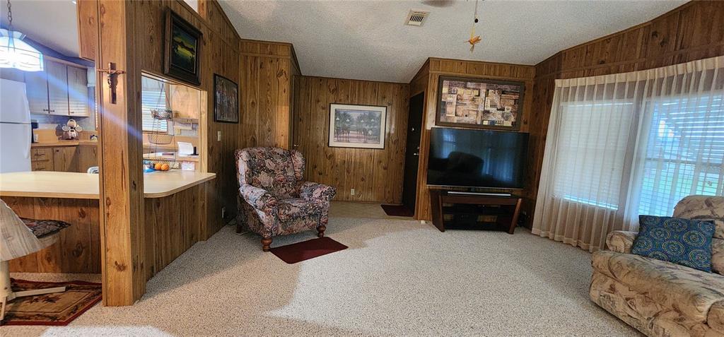 A living room features wood-paneled walls, beige carpeting, a television, and a kitchen pass-through — 2604 MCDANIEL DRIVE, KISSIMMEE, FL