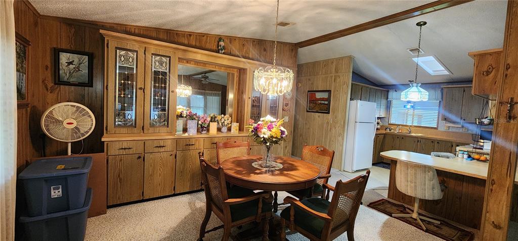 A dining area with wood-paneled walls, a round table, and an adjacent kitchen with cabinets — 2604 MCDANIEL DRIVE, KISSIMMEE, FL