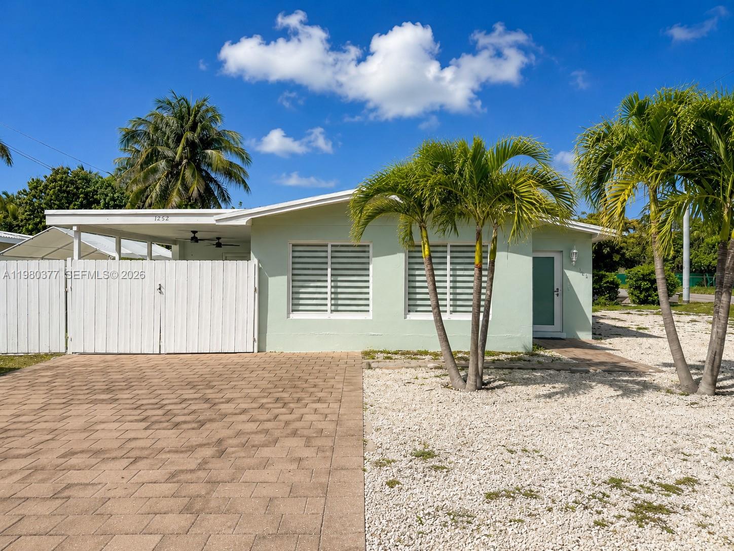 A light green single-story house features a paved driveway, white fence, and palm trees — 1262 Marlin Dr, Marathon FL 33050, MARATHON, FL