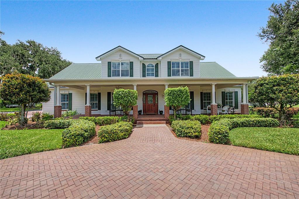 A two-story house with a green metal roof, wrap-around porch, and brick-paved driveway — 3660 FUTCH LOOP, PLANT CITY, FL