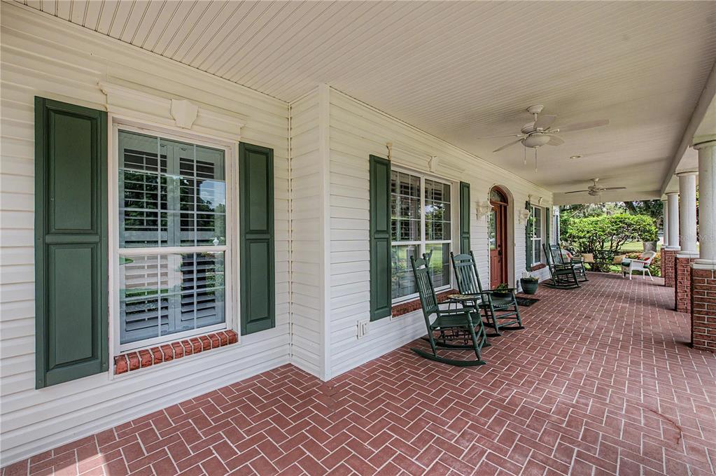 A covered brick porch features white siding, green shutters, and several wooden rocking chairs — 3660 FUTCH LOOP, PLANT CITY, FL