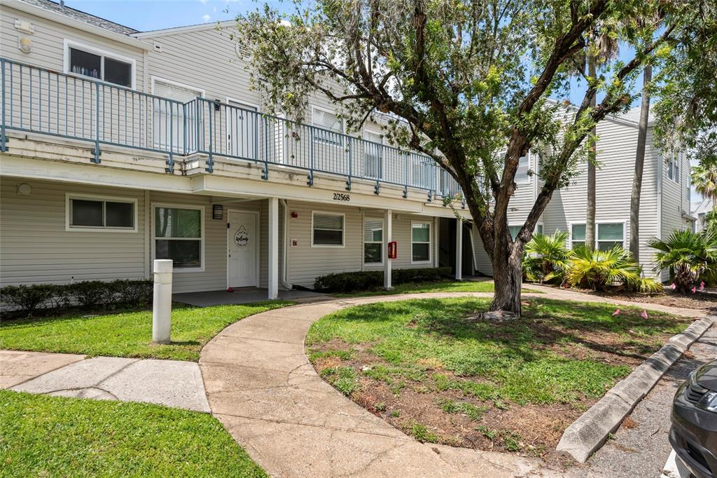 A two-story apartment building with beige siding, a second-floor balcony, and a concrete walkway — 2568 WOODGATE BOULEVARD UNIT 107, ORLANDO, FL