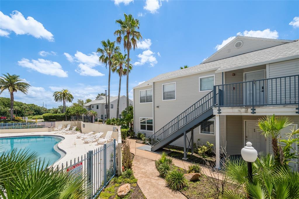 An exterior view of a multi-story apartment building with a swimming pool and palm trees — 2568 WOODGATE BOULEVARD UNIT 107, ORLANDO, FL