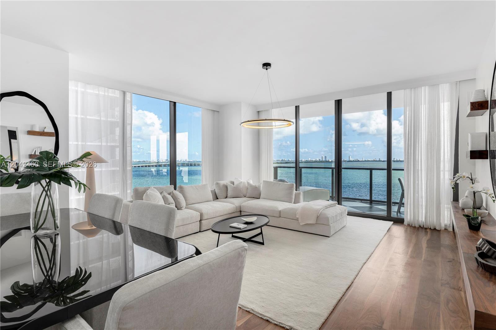 A modern living room features a white sectional sofa, floor-to-ceiling windows, and ocean views — 788 NE 23rd St # 902, Miami FL 33137, MIAMI, FL